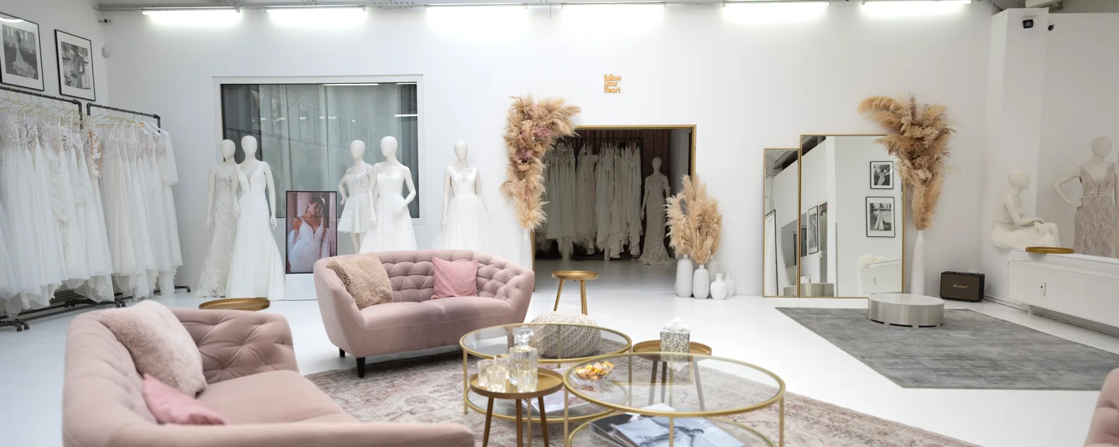 Der Lounge-Bereich im Kleiderloft: rosé Samtsofas um gläserne Beistelltische, dahinter Brautkleider auf Ständern und Mannequins